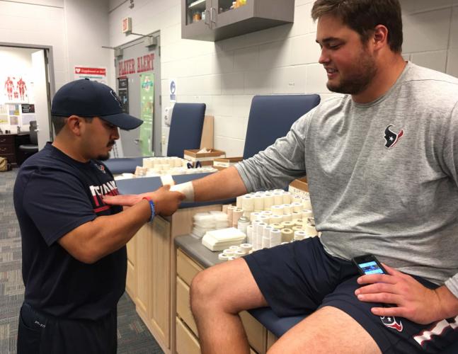 Jeffrey Rodriguez, a Stephen F. Austin State University athletic training graduate student and intern, tapes the wrist of an offensive lineman for the NFL’s Houston Texans.