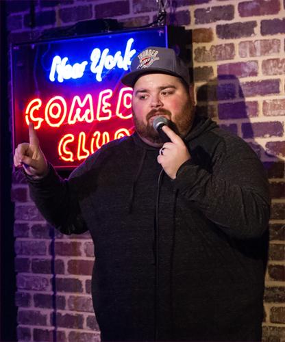 Justin Smith stands on stage in front of a New York Comedy Club neon sign