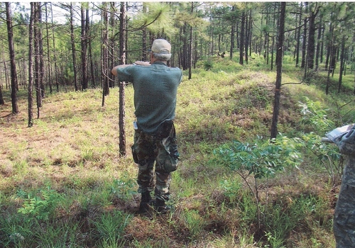 Rickey Robertson showing Fort Polk personnel the site of the Tiger Ridge Village. He is standing on the old berm that ran around the village. At his right foot is one of the old fighting holes used