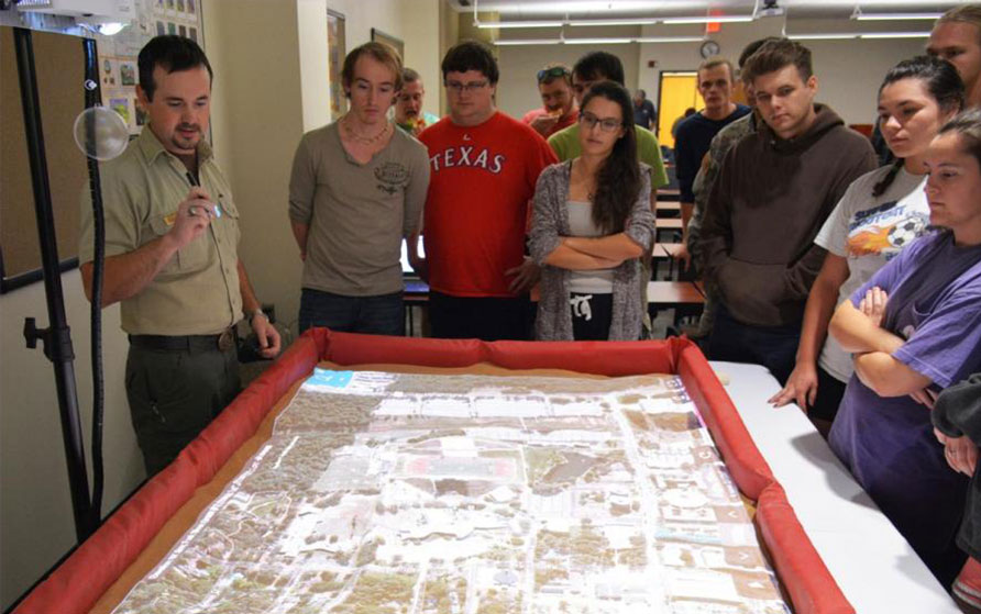 Group of students standing over a table with a map being projected onto it