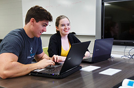 two students working on laptops and smiling