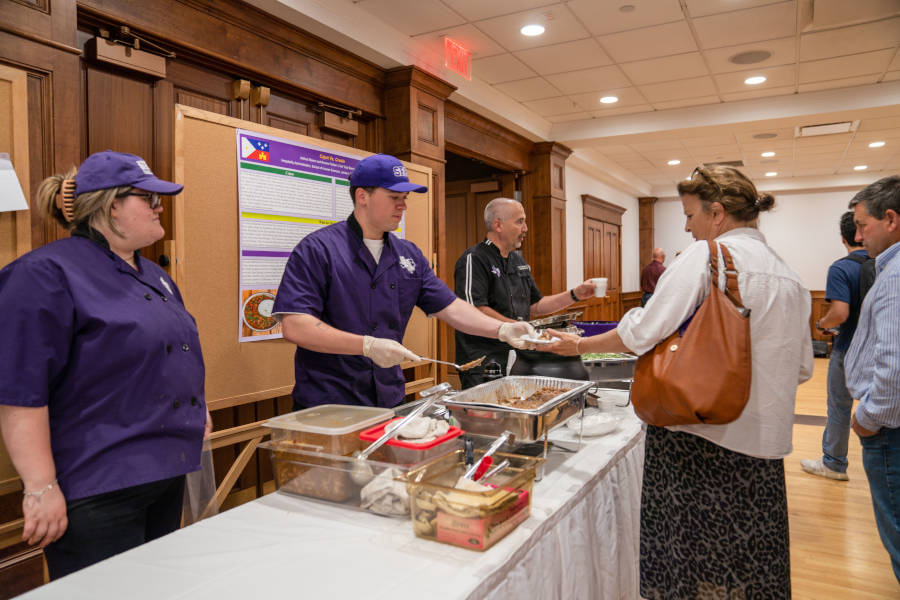 A hospitality administration student demonstrates food services during the Undergraduate Research Conference poster segment.