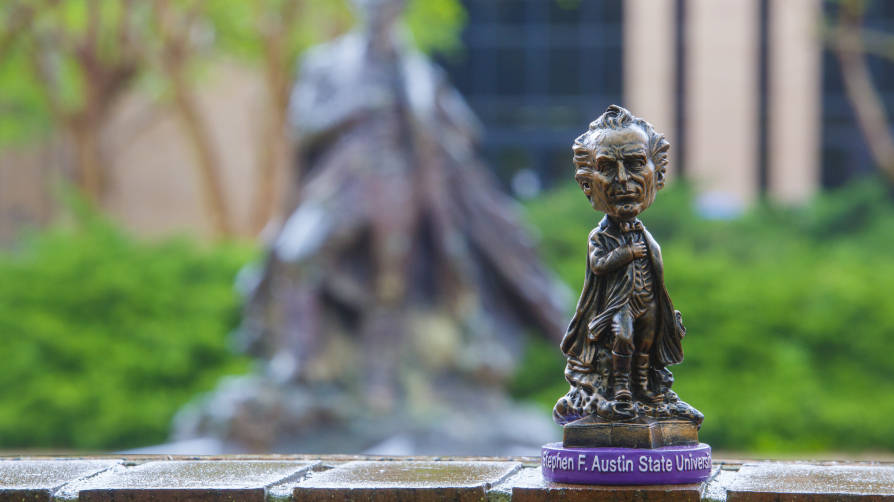 An SFA bobblehead appears in the foreground, with the "Surfin' Steve" fountain sculpture in the background