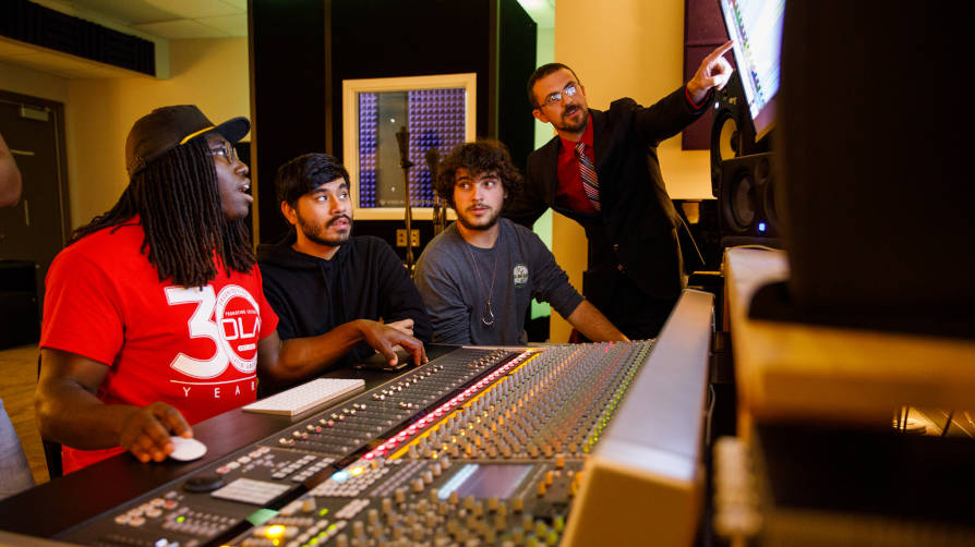A professor guides sound recording technology students in a sound studio lab