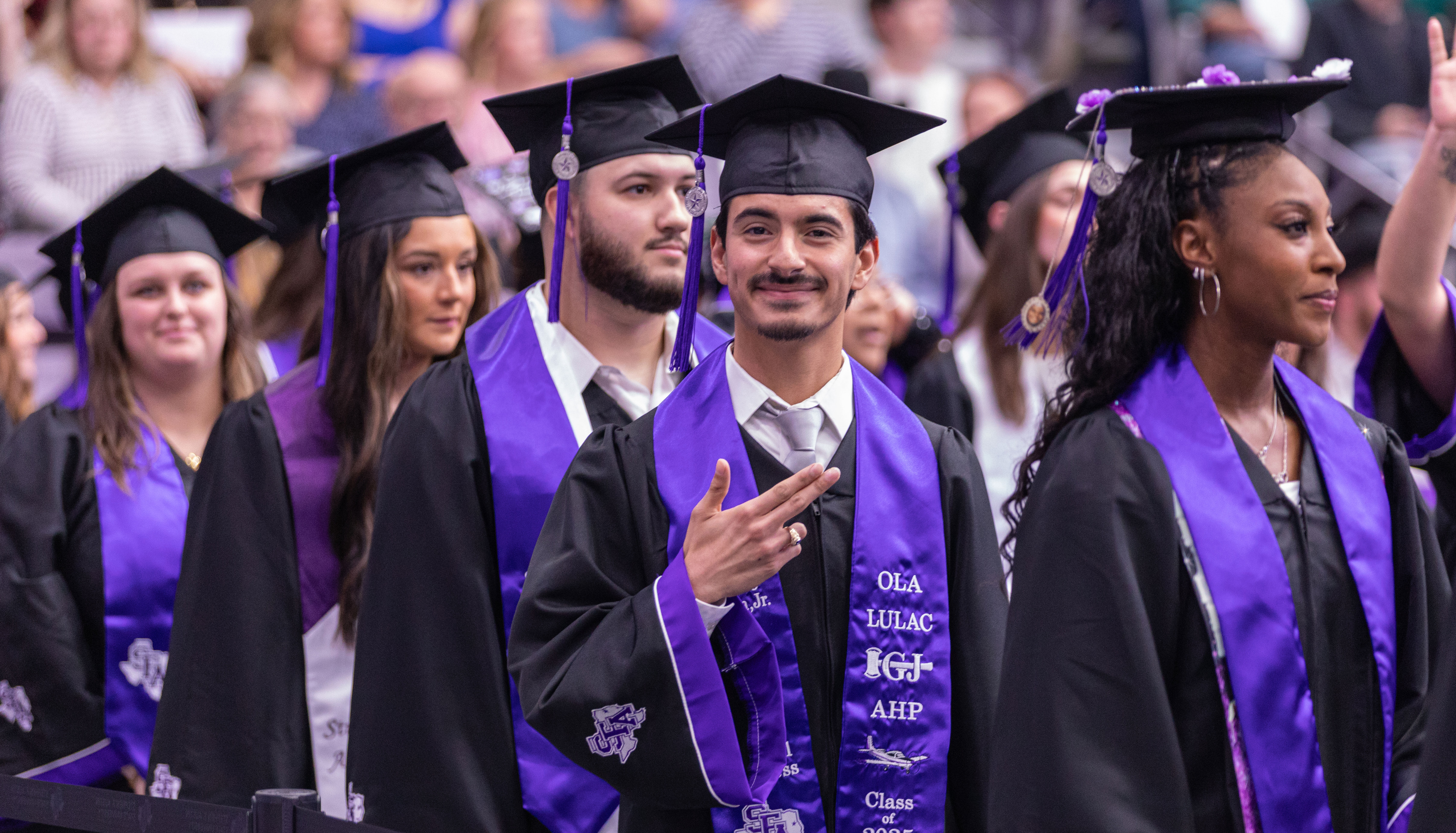 Student smiling at the camera while he walks in line during commencement