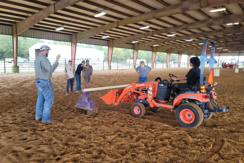 An SFA student practices with heavy machinery under the guidance of faculty members