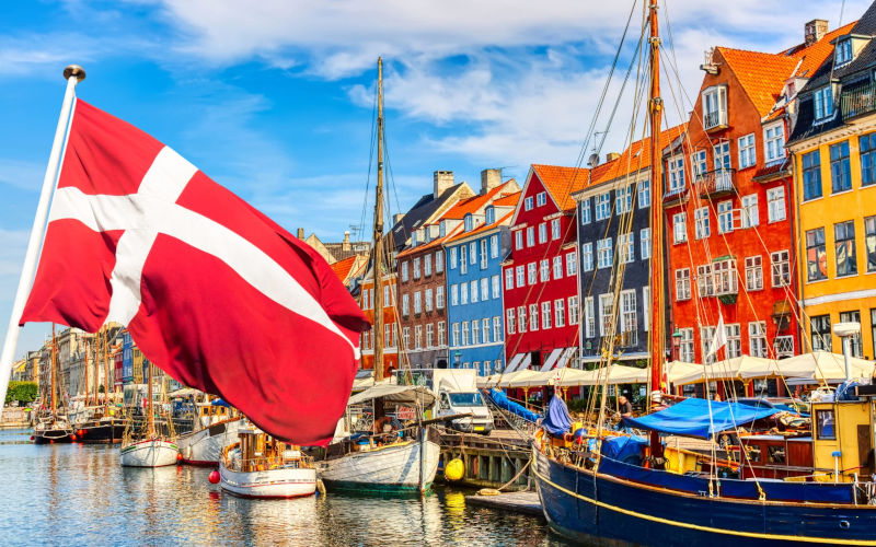 The flag of Denmark is shown against a harbor background with colorful buildings and boats