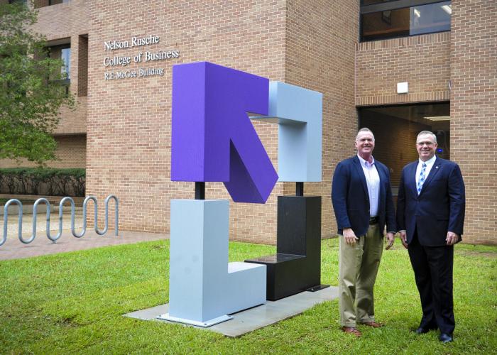Dr. Timothy Bisping and Norman Schippers stand next to a recently unveiled sculpture outside the McGee Business Building on the SFA campus.