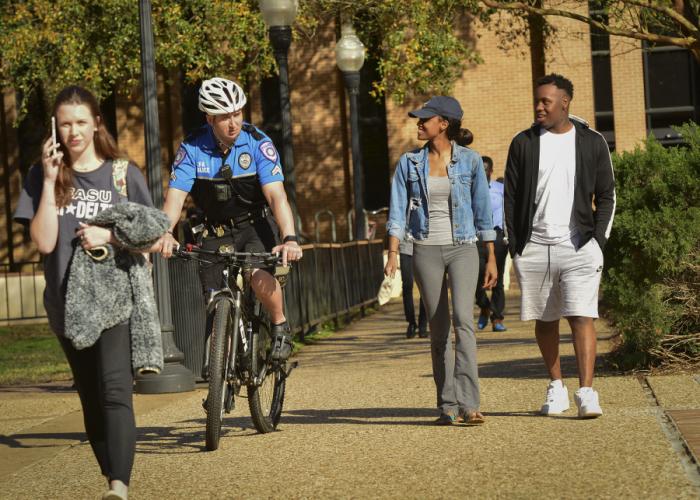 photo of SFA DPS officer riding bike across campus next to students walking