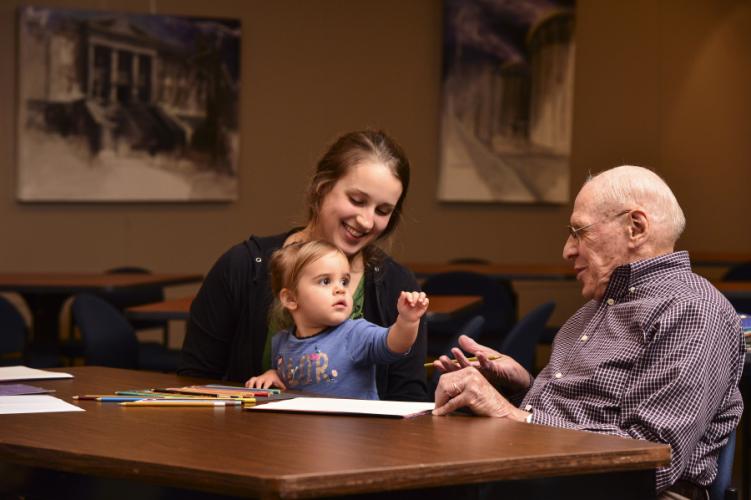 photo of woman holding a toddler and sitting at a table next to an elderly man