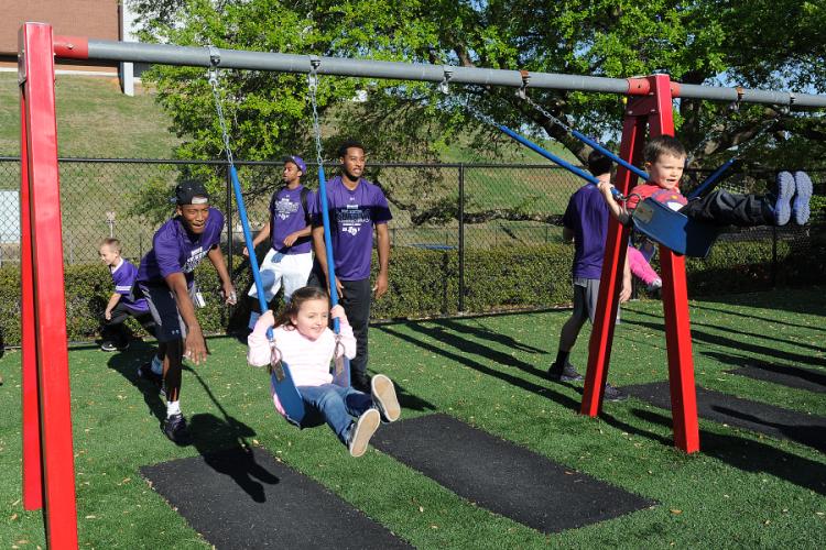 Paisley Cosby and Mason Majors are pushed on the swings by members of the men's basketball team.
