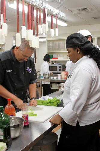 Chef Todd Barrios explains the proper chopping technique to hospitality senior Janice Nelson
