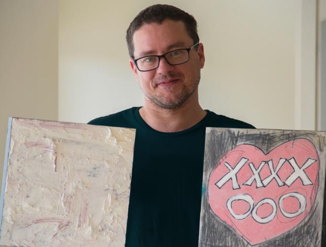 Runcie Tatnall holding to pieces of artwork to be included in the annual 12x12 scholarship fundraiser this year