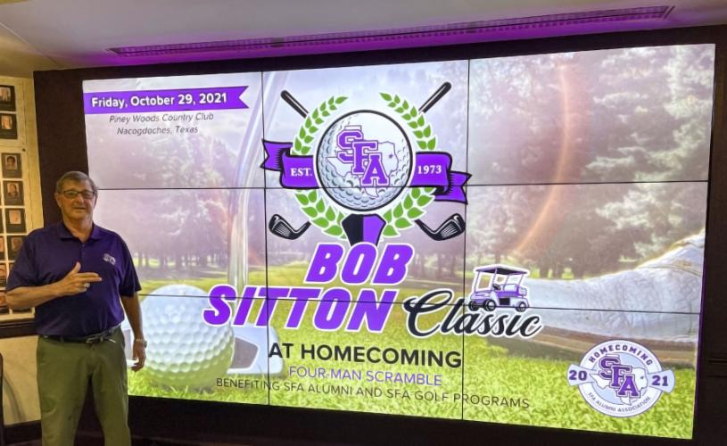 Bob Sitton standing in front of a screen promoting the the Bob Sitton Classic at Homecoming, the golf tournament named in his honor
