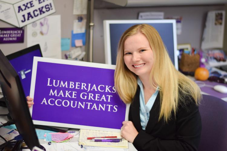 A young woman holding a sign reading, "Lumberjacks MaKe Great Accountants."