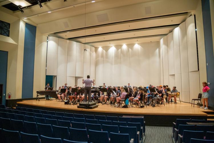 Students rehearse on stage with a conductor
