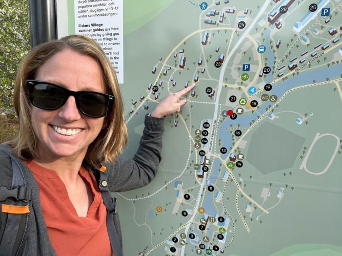 Selden, in front of a map, points to her artist-in-residence home location in Fiskars, Finland.