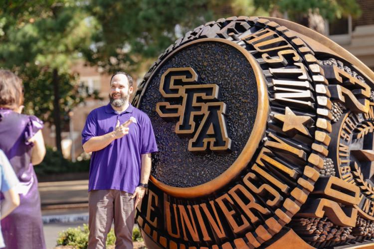 An attendee takes a photo in front of the new Stephen F. Austin State University ring statue during the Centennial Ring Plaza dedication event Monday.