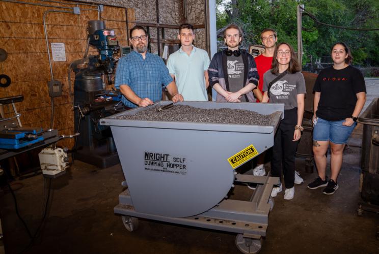 Turner fabrication owner Matt Turner and members of the Economics Reading Group stand next to a fabrication machine.