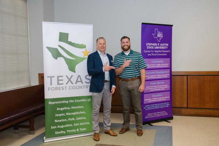 Dr. Mikhail Kouliavtsev and senior economics major Clay Patrick give the axe 'em hand sign while standing in front of CARRI program banners.