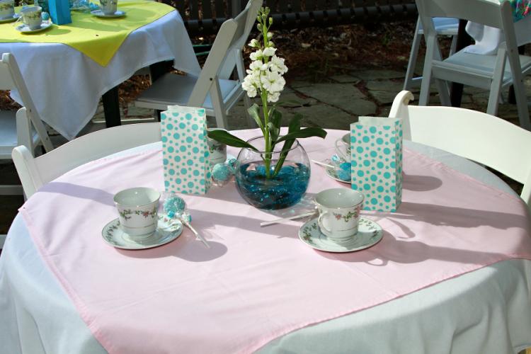 A table top with pastel colors is set with tea cups and decorations.