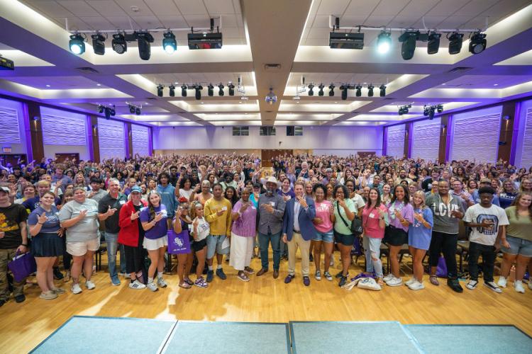 Students, parents and SFA members showing the "axe 'em" hand sign crowd a large hall with purple lights in the background