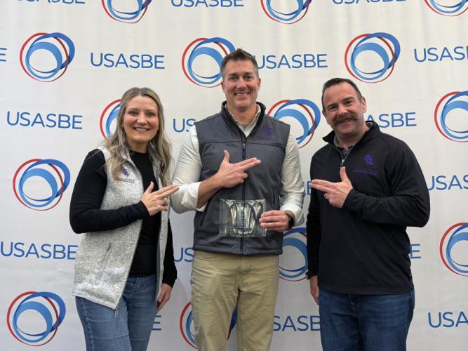Dr. Hollie Gammel Smith, Dr. Raymond Jones and Matt Smilor display their award while standing in front of a USASBE backdrop