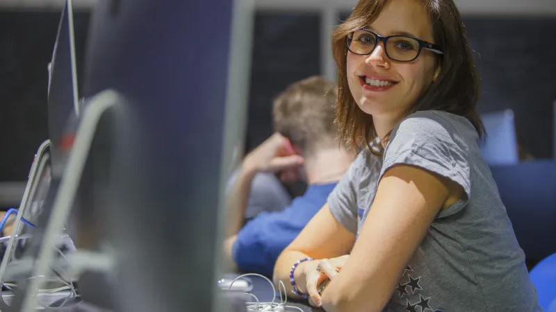 Student smiling at the camera while she sits in front of a computer