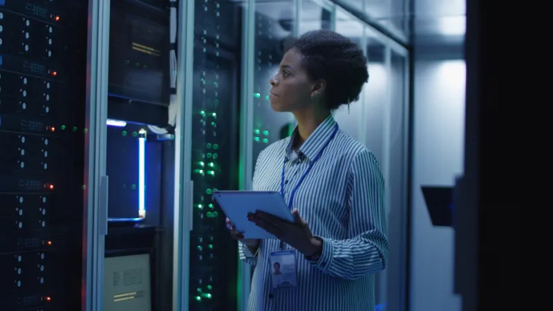 Portrait of African American woman working as IT engineer and standing among server racks in data center room