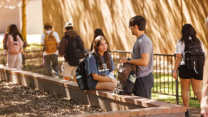 Two students having a conversation outside while others walk past