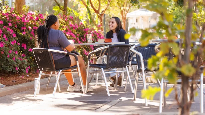 Two female students sitting at a table outside while they talk