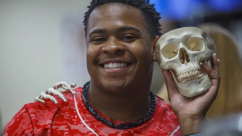 Student smiling at the camera and posing with a skeleton