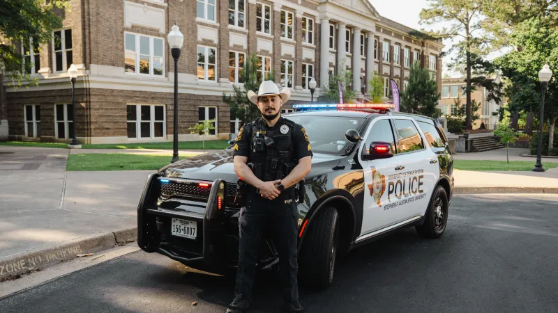 university police officer poses in front of his cruiser