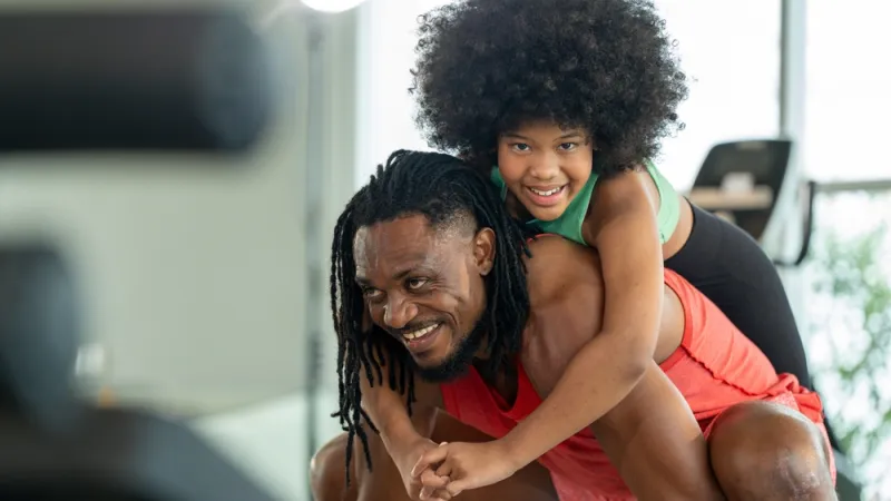 Adult squatting with child smiling and wrapping arms around adult's neck