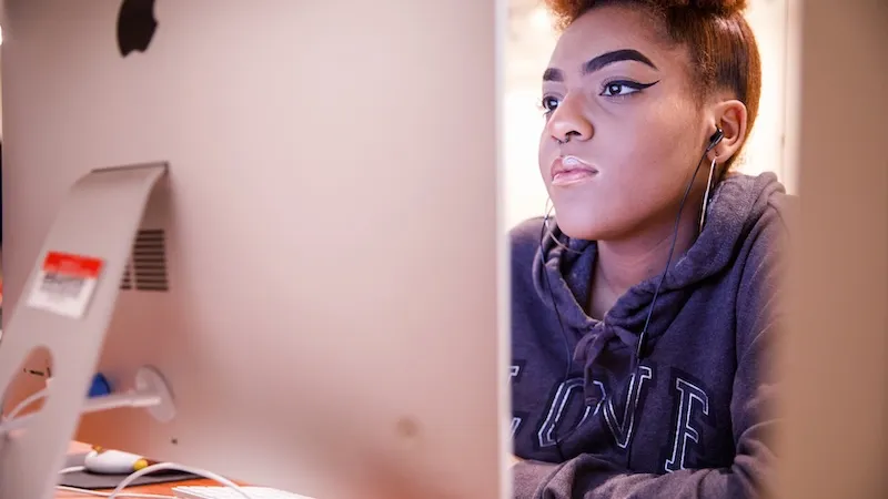 Student sitting at computer working with earbuds in