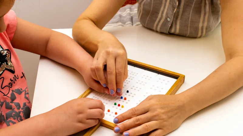 Teacher working with a student to learn braille alphabet