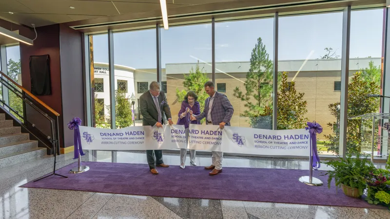 Standing on a purple carpet with a windowed backdrop of trees, Priscilla “Prissy” Abshier Sliva is assisted by Dr. Gary Wurtz and Dr. Neal Weaver in cutting a ceremonial ribbon.