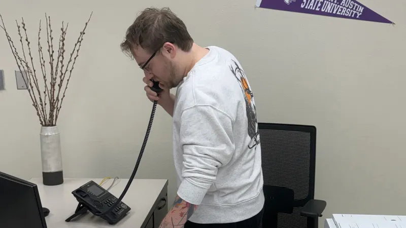 Kyle Sinopoli takes a sales phone call in an office with an SFA pennant in the background