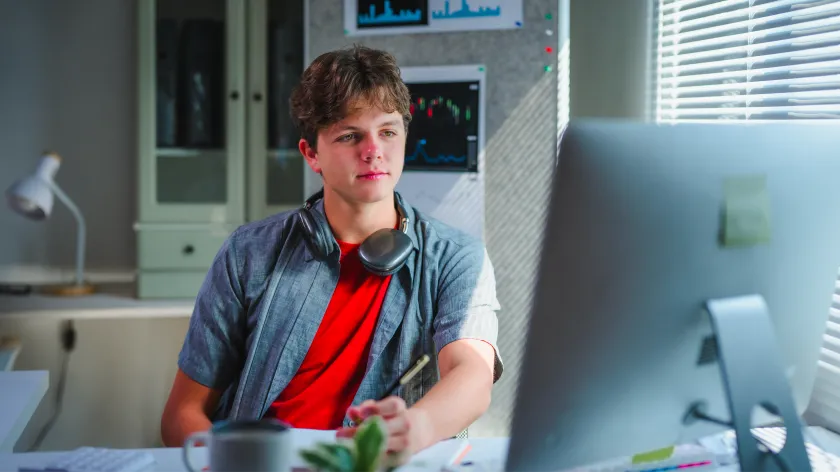 stduent wearing headphones around neck sits in from of computer in home office