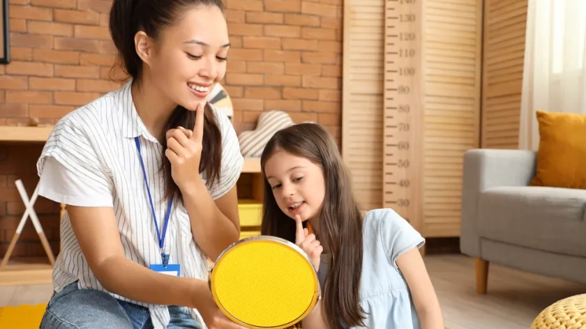 speech therapist and little girl with mirror pronouncing letters in office