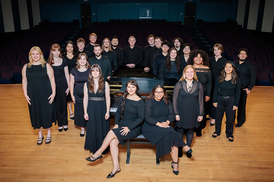 Chamber singers gathered around piano on the stage of Cole Concert Hall