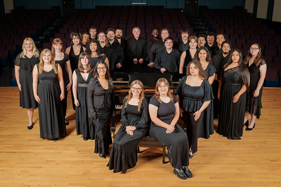 Chamber singers gathered around piano on the stage of Cole Concert Hall