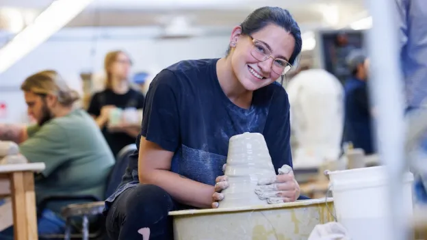 Student smiling at camera while working with clay