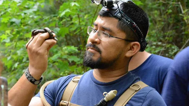 Student holding a small snake in the forest