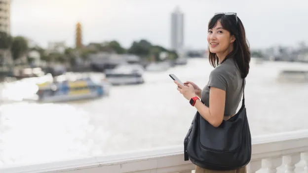 Woman exploring the world smiling while she stands on a bridge overlooking a river