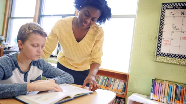 Teacher, boy and reading in classroom with textbook for learning literature
