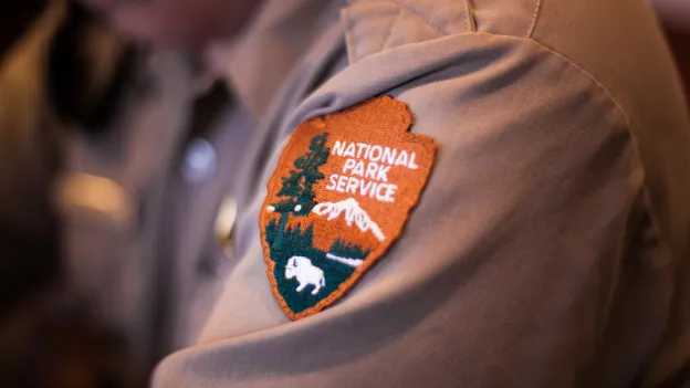 Badge with the Logo of the National Park Service on a Shirt of a Ranger