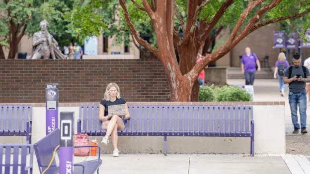 Female student sitting on a purple bench outside while she works on her laptop
