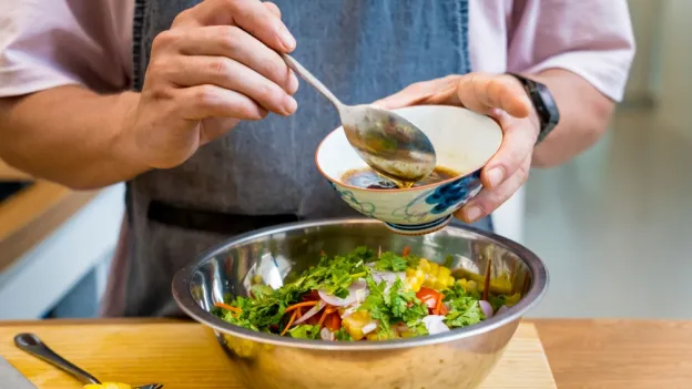 closeup of person preparing to use a spoon to add dressing to a salad