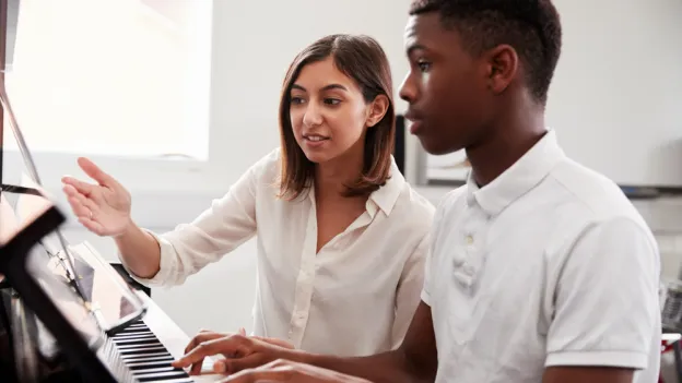 Male Pupil With Teacher Playing Piano In Music Lesson